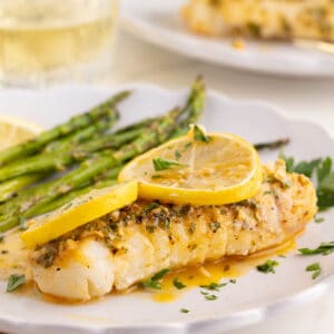 Lemon garlic baked cod on a white plate with asparagus and lemon slices