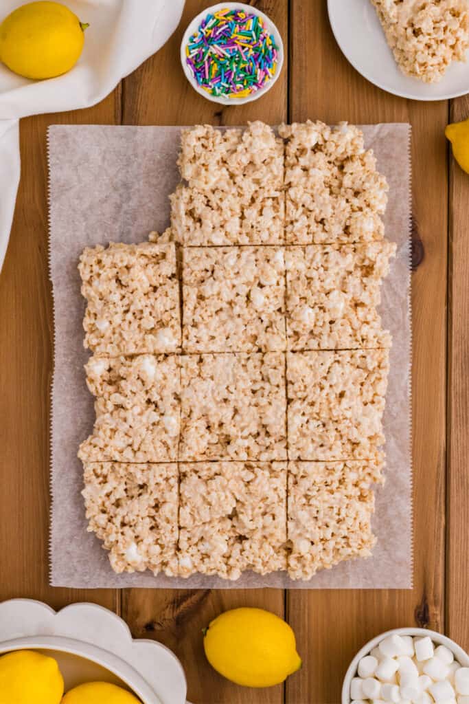cut lemon rice crispy treats arranged on parchment paper with lemons and sprinkles around them