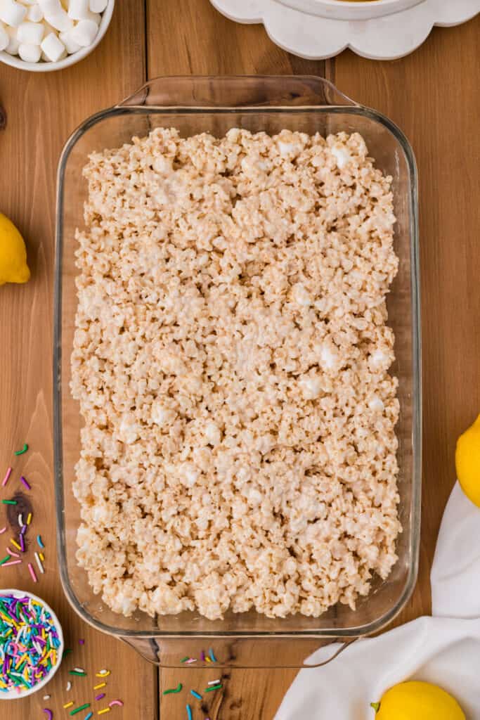 rice crispy treat mixture pressed into a glass baking dish with lemons and sprinkles nearby