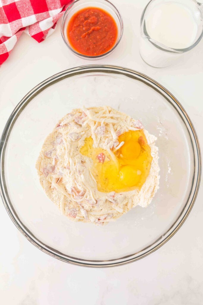 eggs added to the flour, cheese, and pepperoni mixture in a glass mixing bowl