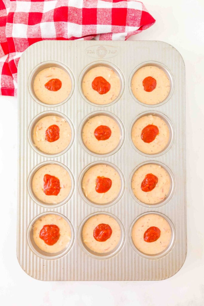 muffin pan filled with pizza muffin batter topped with small dollops of pizza sauce