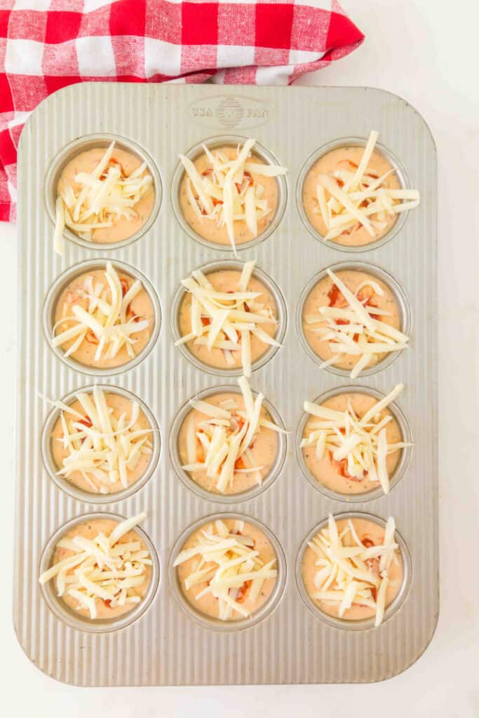 muffin pan filled with pizza muffin batter topped with shredded mozzarella cheese