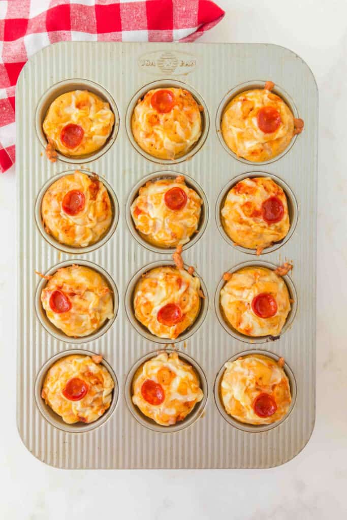 baked pizza muffins in a muffin pan topped with melted cheese and pepperoni slices