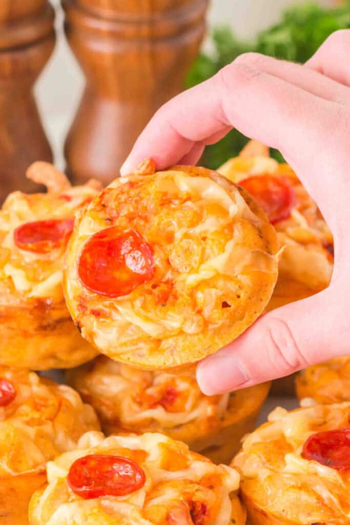 hand holding a baked pizza muffin topped with melted cheese and pepperoni