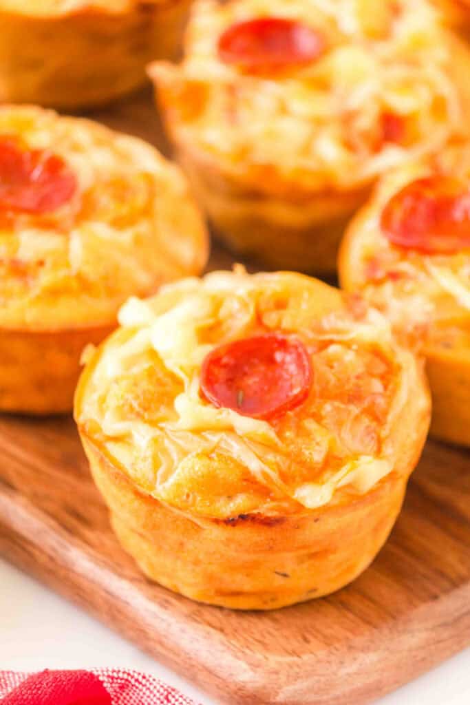 close-up of baked pizza muffins with melted cheese and pepperoni on a wooden board