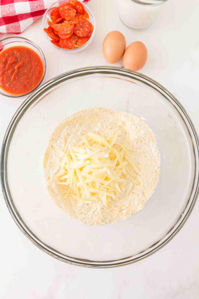shredded mozzarella cheese added to a bowl of flour and cornmeal mixture