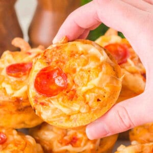 square image of a hand holding a pizza muffin topped with melted cheese and pepperoni