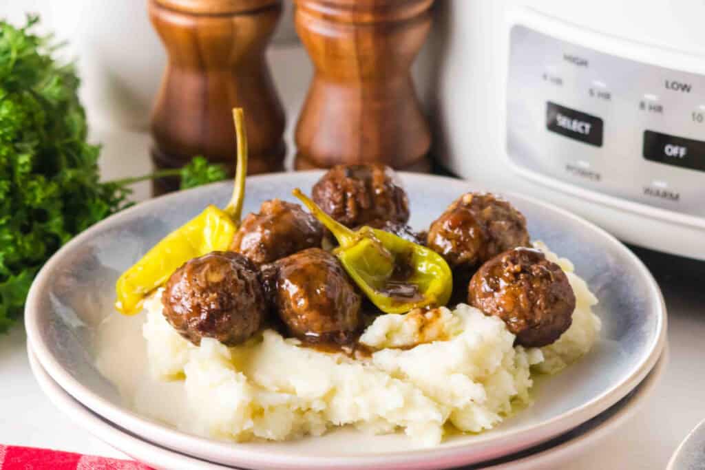 slow cooker mississippi meatballs on mashed potatoes on a plate near a slow cooker