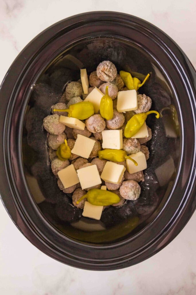 frozen meatballs in a slow cooker with pepperoncini and butter added on top