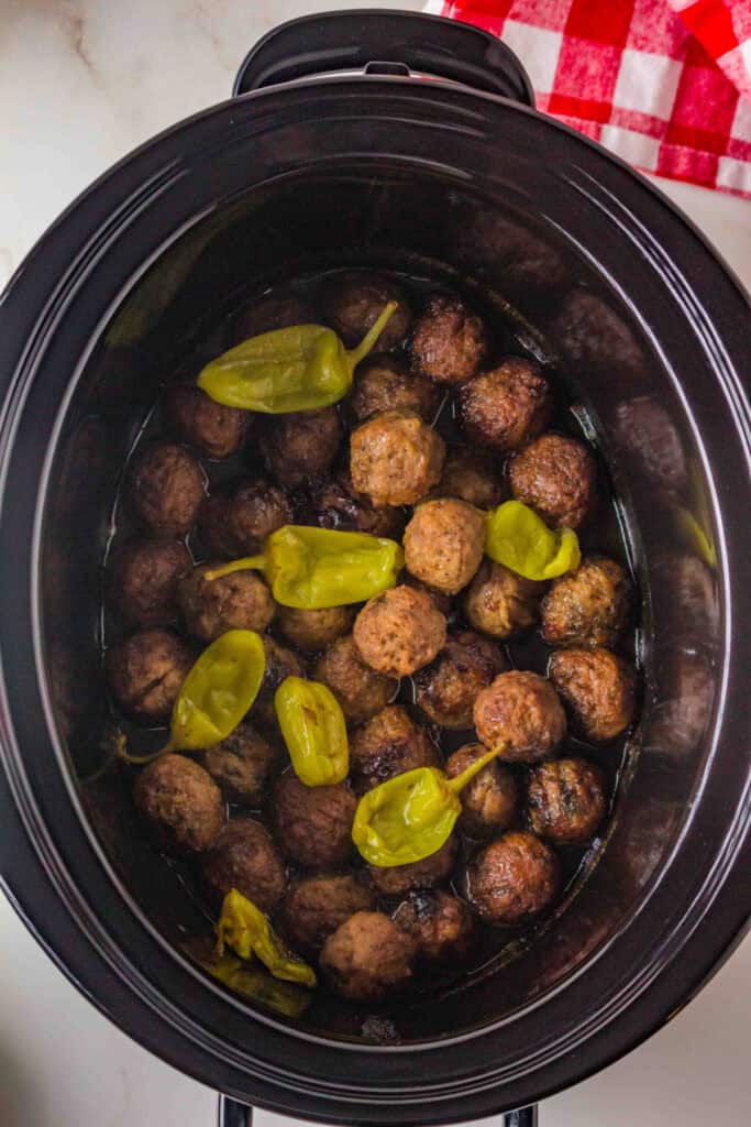 cooked meatballs in sauce inside a slow cooker with pepperoncini peppers