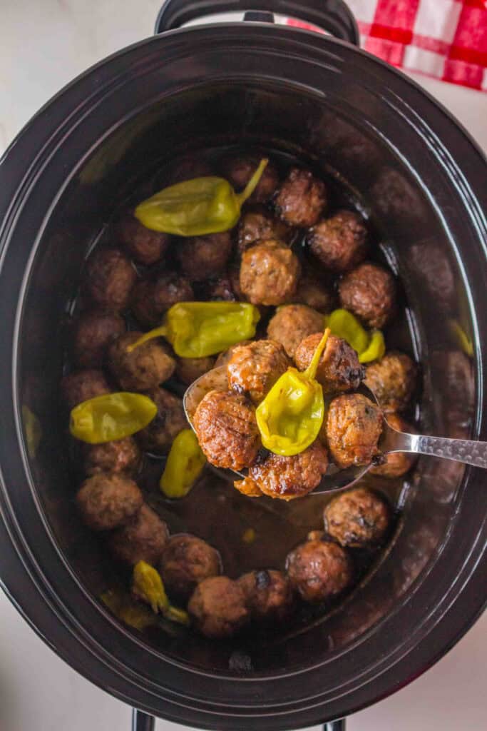 spoon lifting saucy slow cooker meatballs with a pepperoncini from the slow cooker