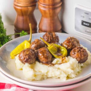 slow cooker mississippi meatballs with pepperoncini served over mashed potatoes on a plate near a slow cooker