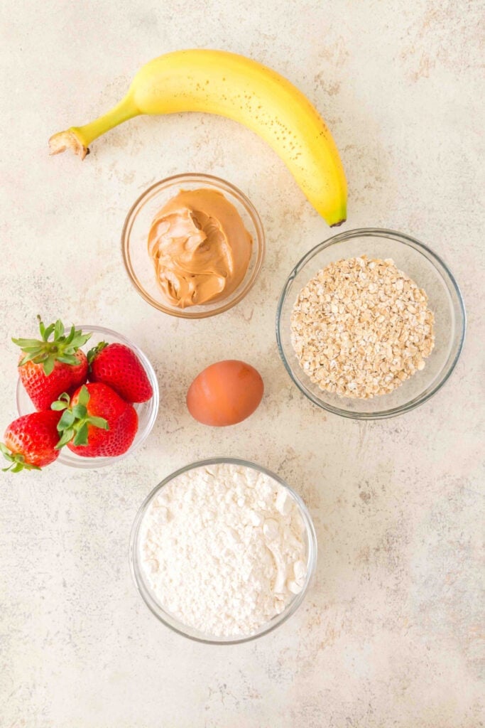 banana, strawberries, peanut butter, oats, flour, and a large egg arranged on a light countertop
