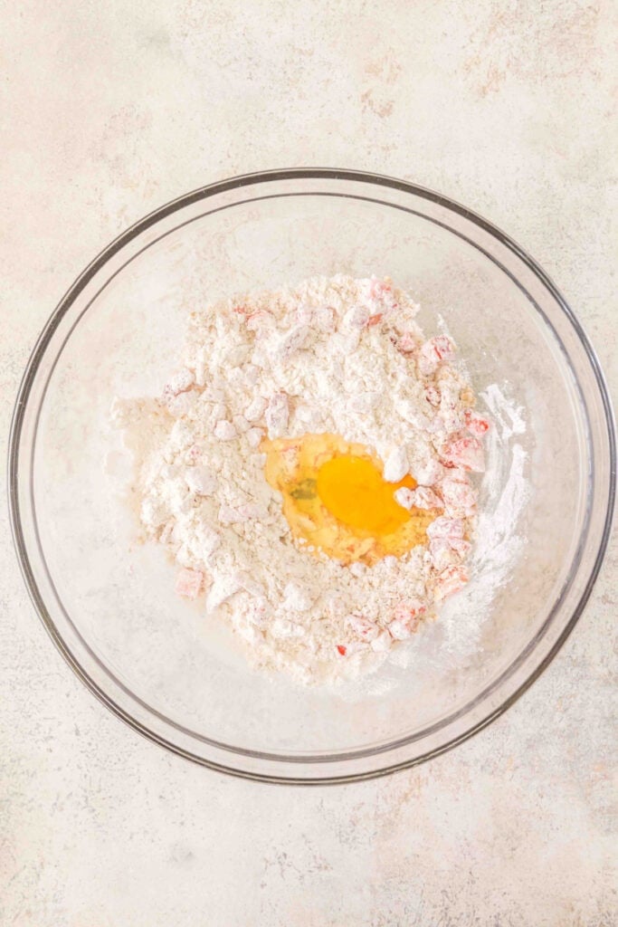 flour mixture with chopped strawberries in a bowl with a cracked egg added
