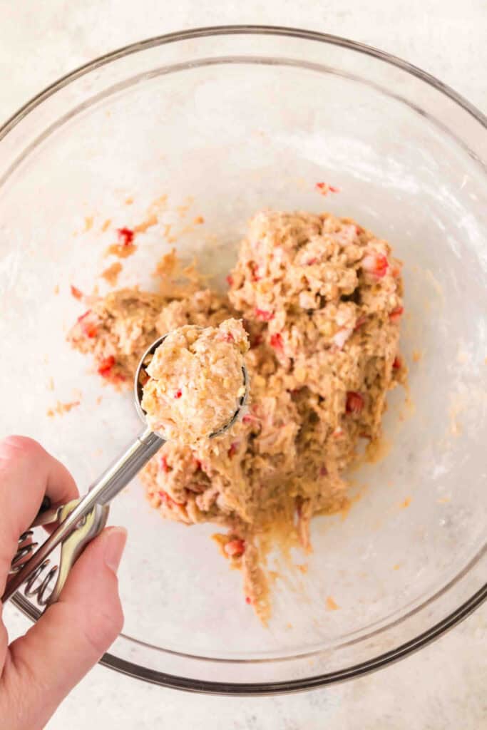 scoop of strawberry banana dog treat dough held over a mixing bowl