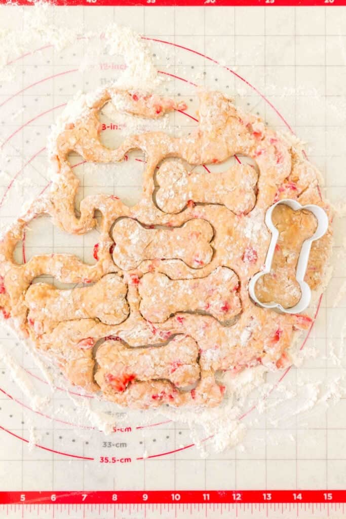 rolled dog treat dough with strawberry pieces cut into bone shapes on a floured baking mat