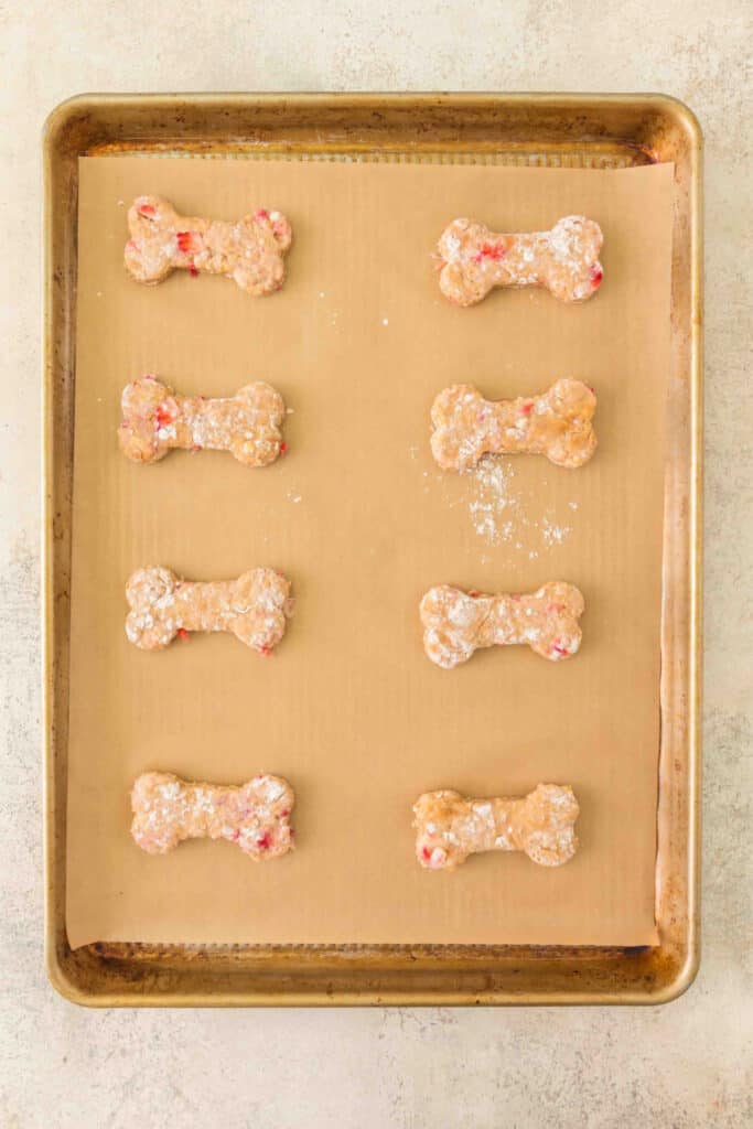 unbaked strawberry banana dog treats shaped like bones on a parchment-lined baking sheet