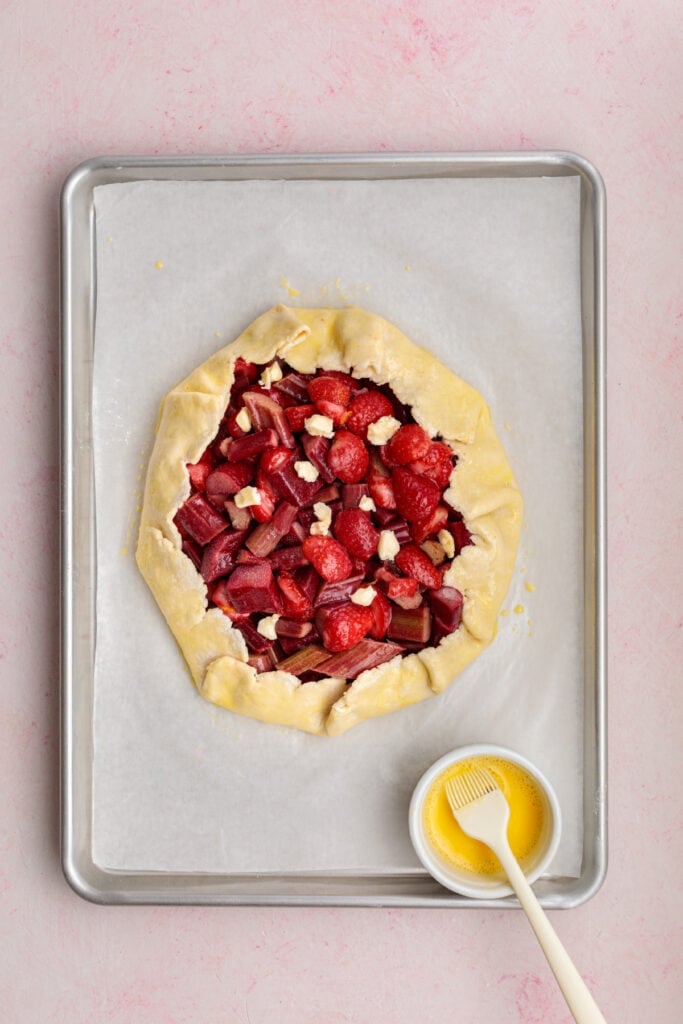 galette brushed with egg wash with a small bowl and pastry brush on the baking sheet