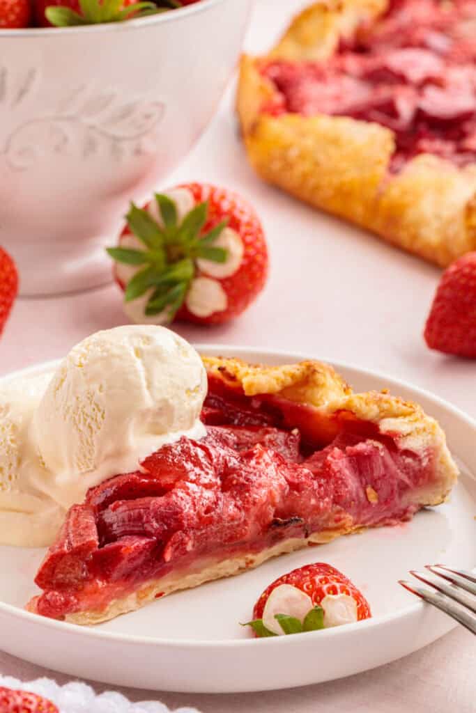 slice of strawberry rhubarb galette served on a plate with a scoop of vanilla ice cream and fresh strawberries