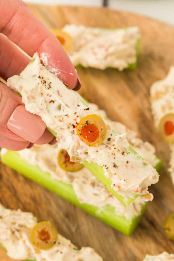 hand holding a piece of stuffed celery topped with a sliced olive and black pepper
