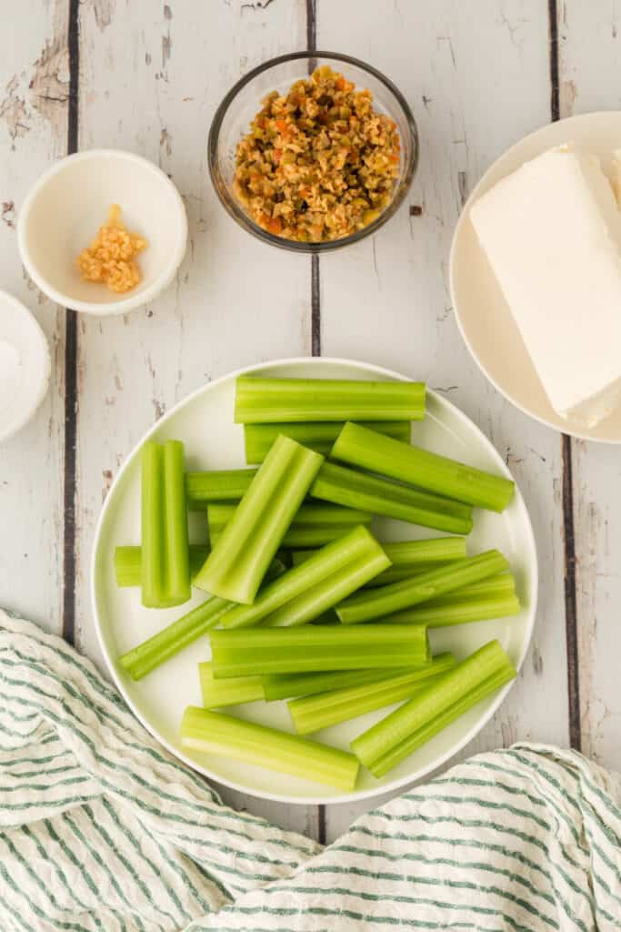 cut celery pieces arranged on a plate with cream cheese, chopped olives, and garlic nearby