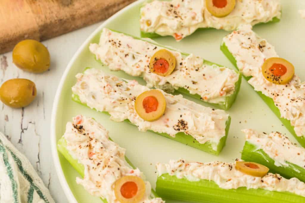 close up of stuffed celery on a plate topped with sliced olives and black pepper