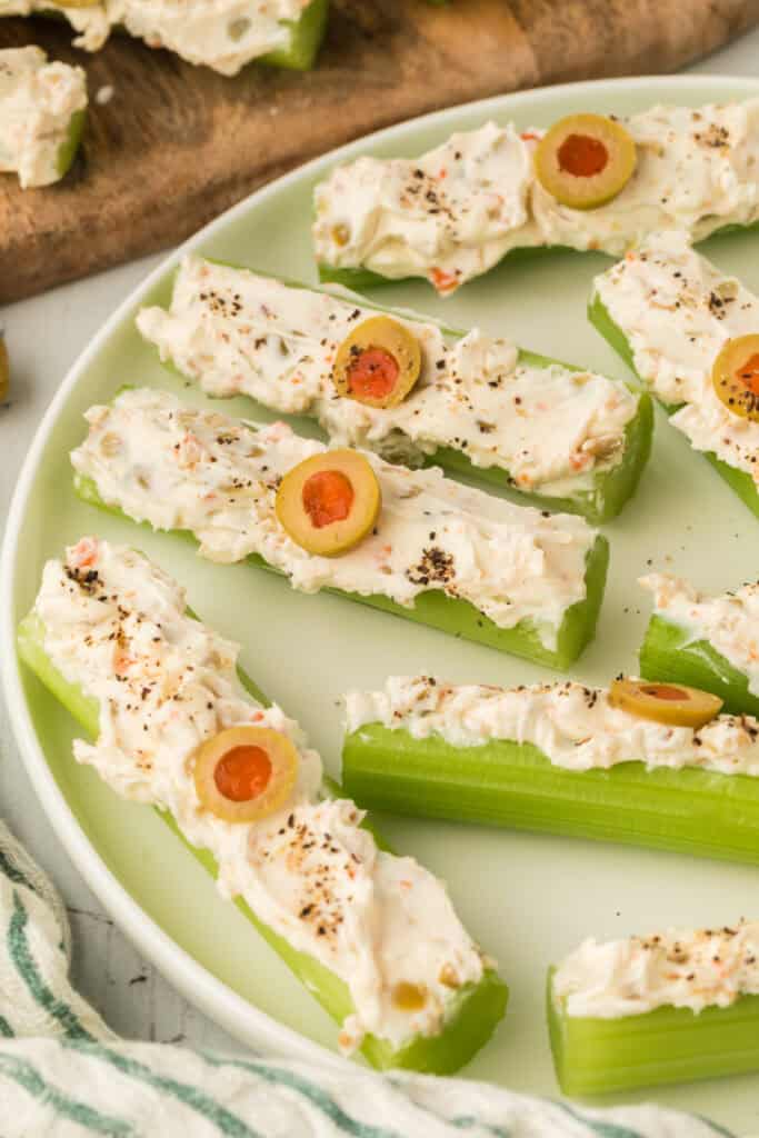 close up of stuffed celery sticks with cream cheese filling, olives, and black pepper on a plate