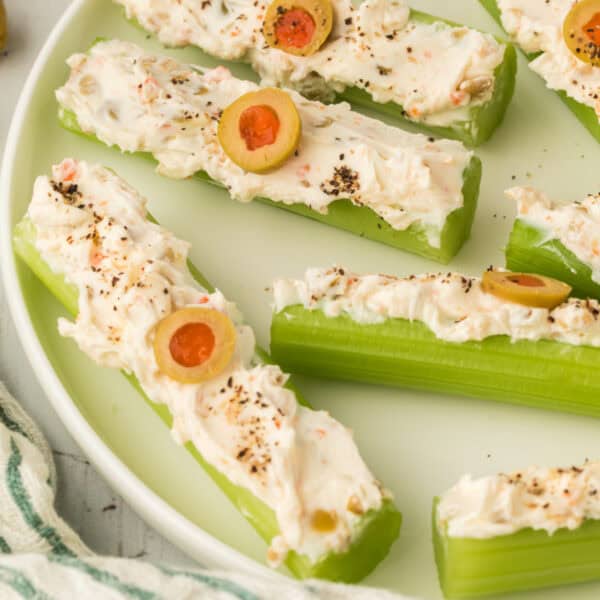 close up of stuffed celery sticks on a plate topped with cream cheese filling, sliced olives, and black pepper