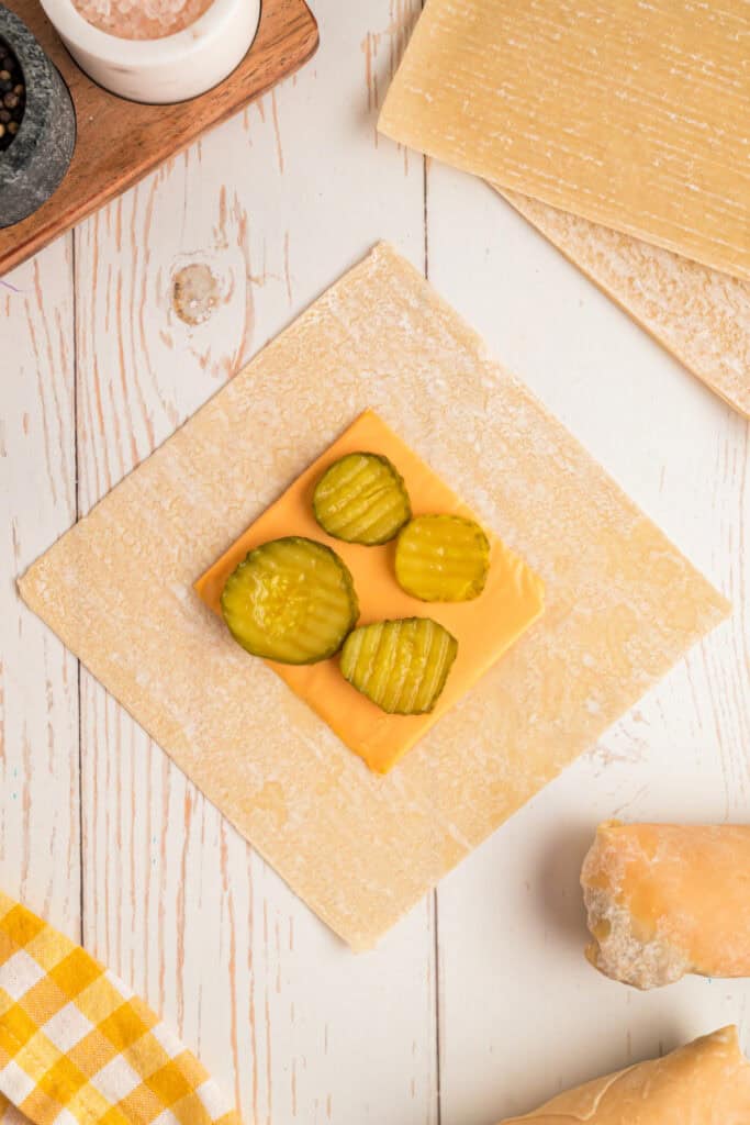 pickle slices placed on American cheese on egg roll wrapper for Big Mac Egg Rolls
