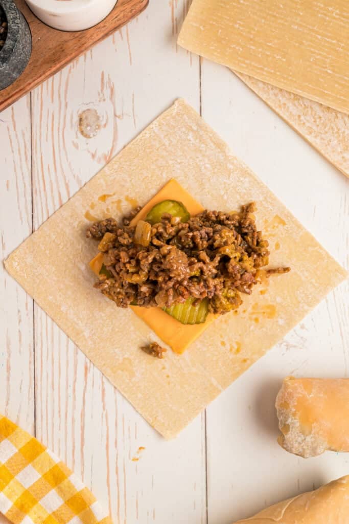 ground beef mixture added on top of cheese and pickles on wrapper for Big Mac Egg Rolls