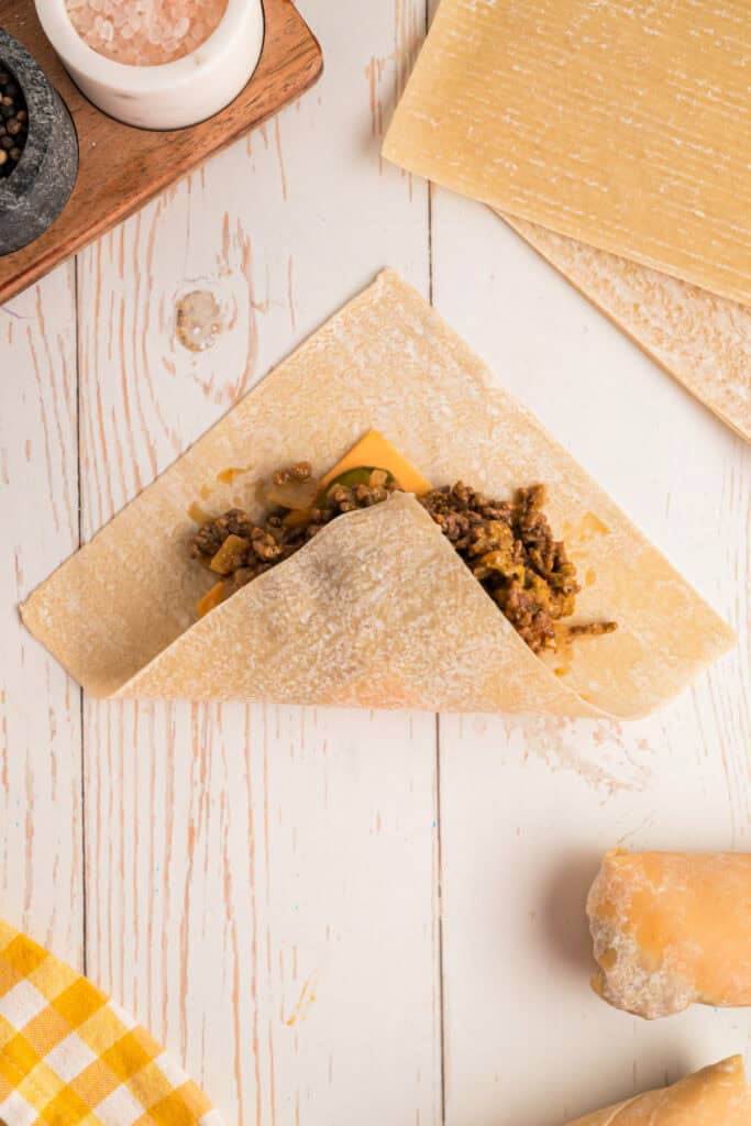 bottom corner of egg roll wrapper folded over filling for Big Mac Egg Rolls