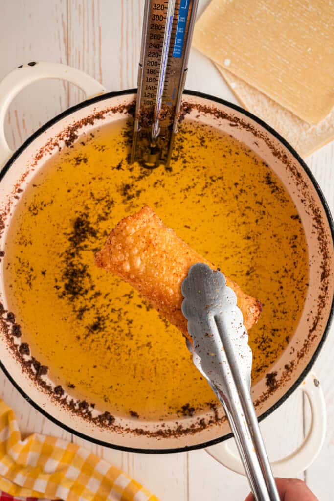 cooked Big Mac Egg Roll held with tongs above hot oil