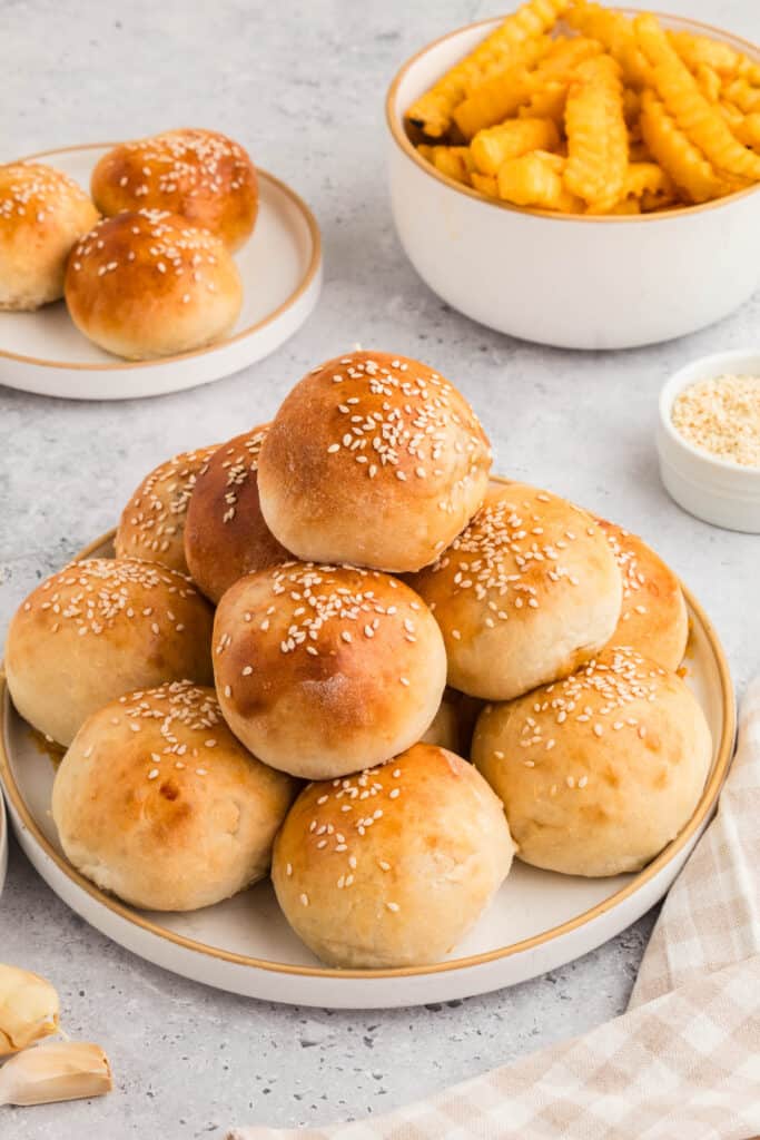 plate of baked burger bombs with sesame seeds and a bowl of fries in the background