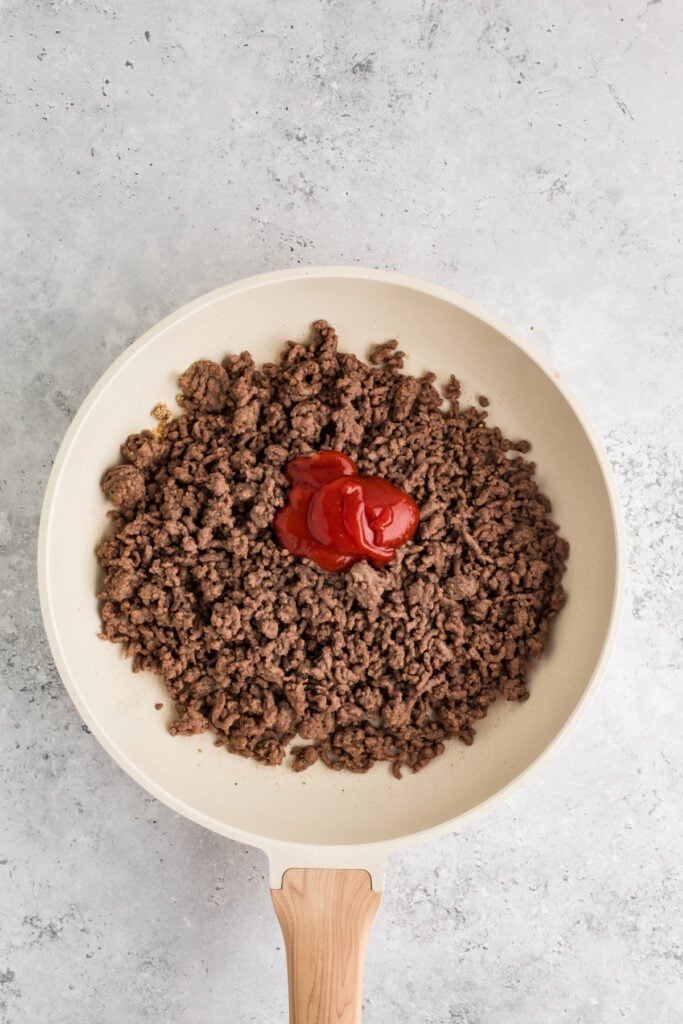 cooked ground beef in a skillet with ketchup added on top