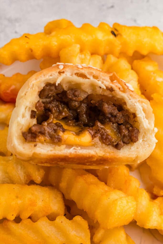 half of a burger bomb with ground beef and melted cheese served with crinkle cut fries in the background