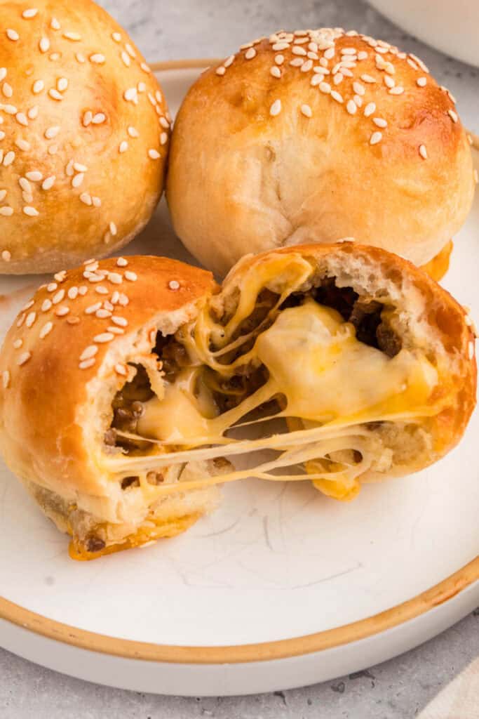 burger bombs on a plate with one cut open showing melted cheese and ground beef filling