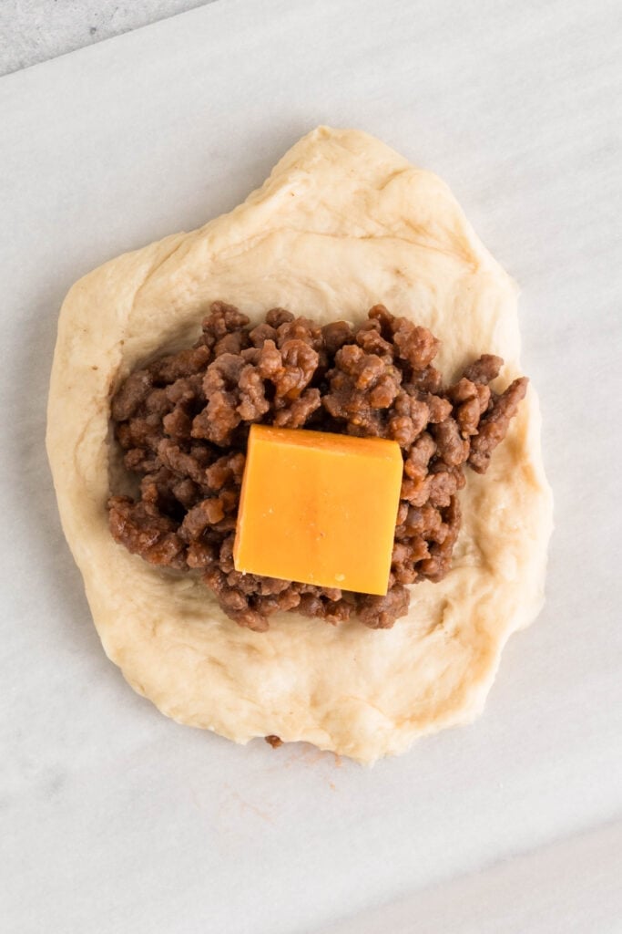 flattened dough with cooked ground beef and a cube of cheddar cheese in the center