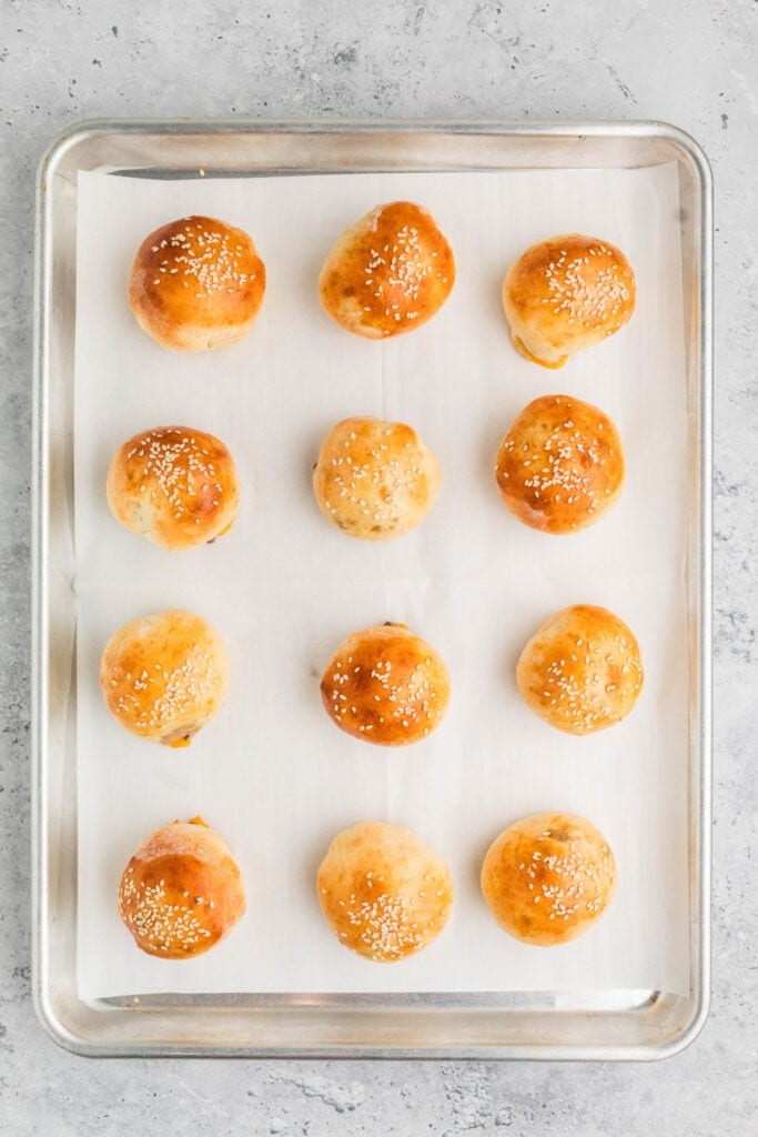 baked burger bombs with sesame seeds on a baking sheet