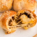 close-up of a burger bomb split open with melted cheese stretching and sesame seeds on top