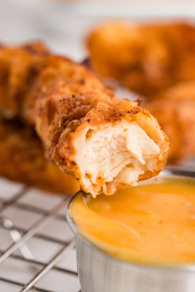 close up of a fried chicken strip dipped in sauce showing the inside texture