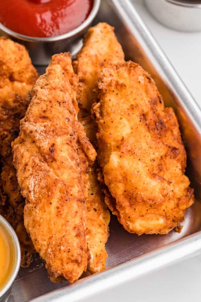 close up of crispy fried chicken strips on a tray with dipping sauces