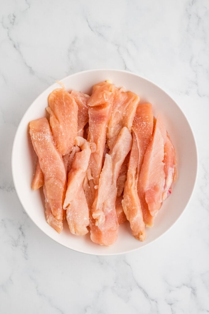 raw chicken strips in a bowl sprinkled with salt