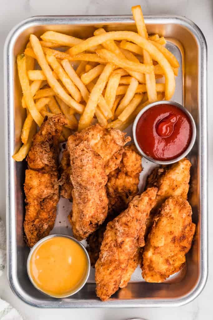 ried chicken strips served with fries and ketchup in a metal tray