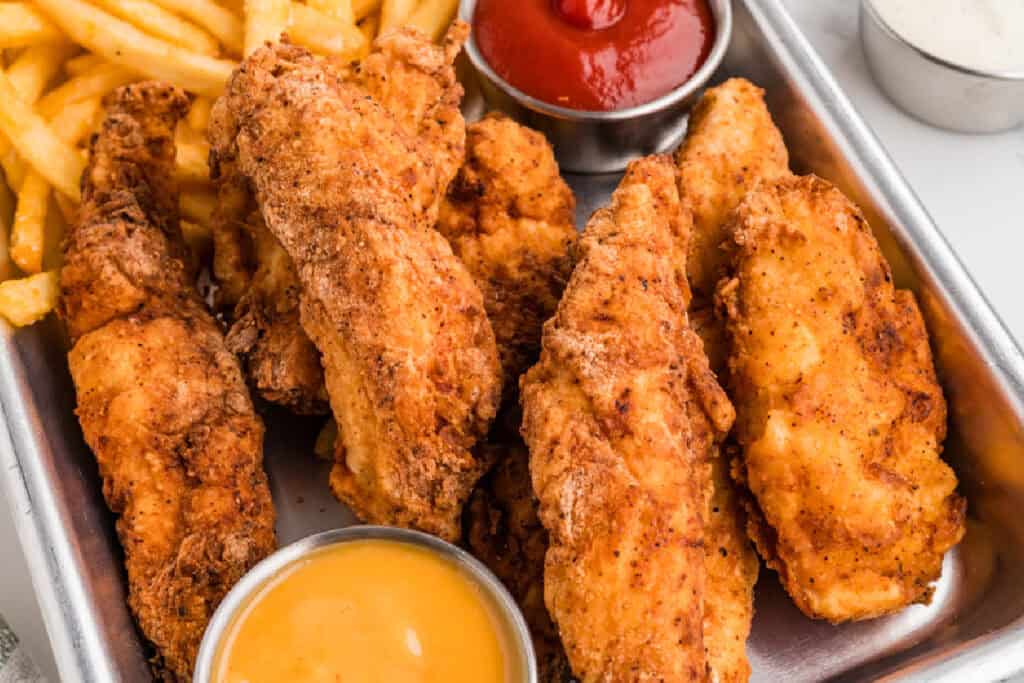 crispy fried chicken strips with fries and dipping sauces on a tray