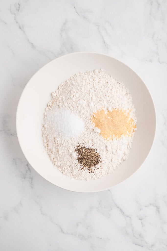 flour in a bowl with salt, pepper, and seasoning added on top