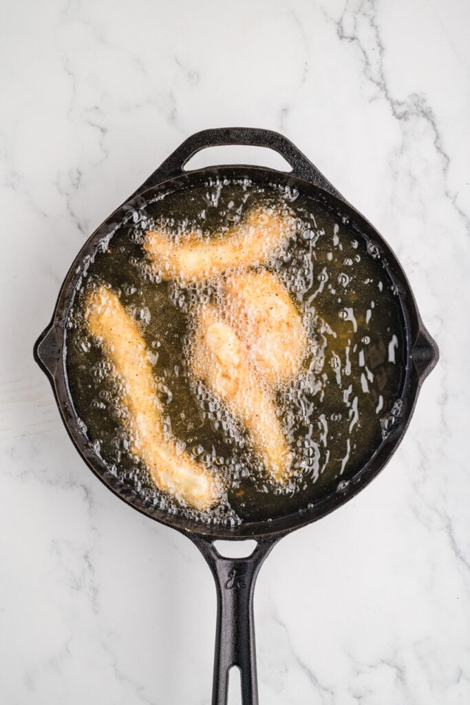 chicken strips frying in hot oil in a cast iron skillet