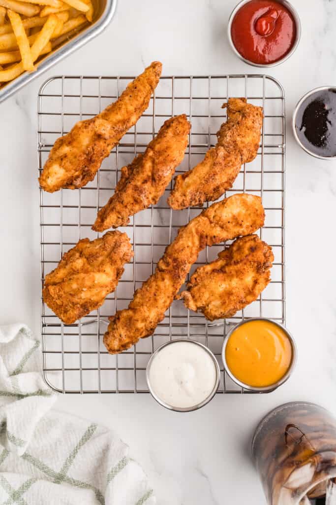fried chicken strips on a wire rack with dipping sauces and fries