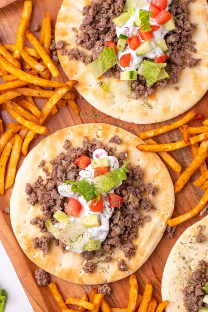 pita breads topped with ground beef, yogurt sauce, cucumber, tomato, and lettuce served with fries