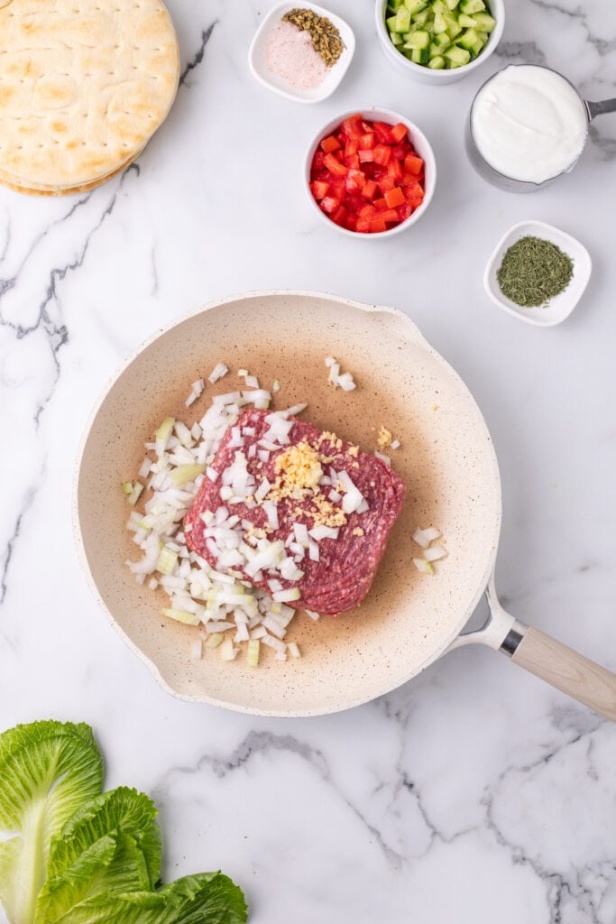 raw ground beef with chopped onion and minced garlic in a skillet on a marble surface