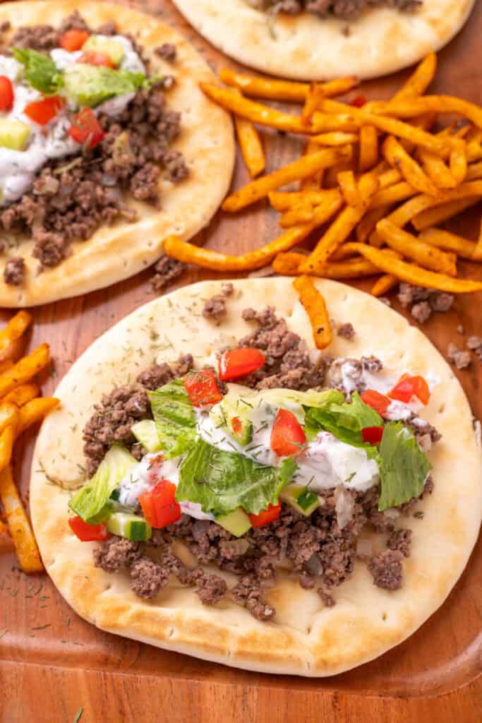 close view of pita bread topped with ground beef, yogurt sauce, cucumber, tomato, and lettuce